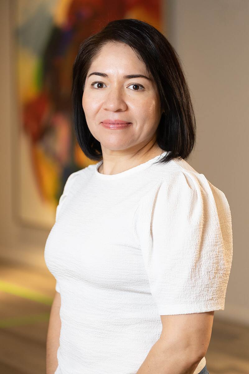 Professional portrait of Cecilia Juarez from Triple A Restaurant Group, wearing a white blouse and smiling in a modern office environment — representing reliability, teamwork, and dedication in hospitality operations.