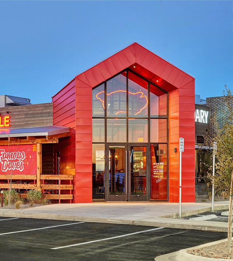Front entrance of Famous Dave’s BBQ featuring bold red architecture and a neon pig sign—welcoming guests to a fun, casual dining experience centered around award-winning barbecue flavors.
