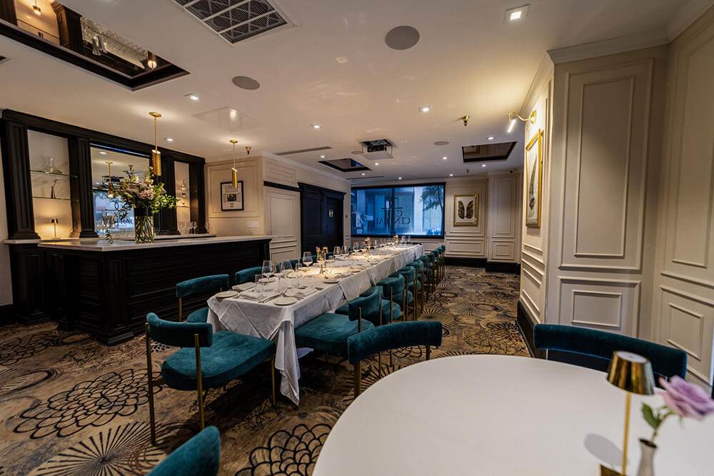 Elegant private dining room at Café Central, featuring a long white-tableclothed table with teal velvet chairs, gold-accented lighting, and a classic bar—ideal for intimate gatherings, upscale celebrations, and fine dining events in El Paso.